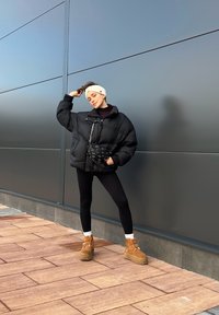 Must mustela jope, must leggings, beežid platvormkingad. Aksessuaarideks on must ristiõlakott, millel on augud ja heledat värvi peapael.