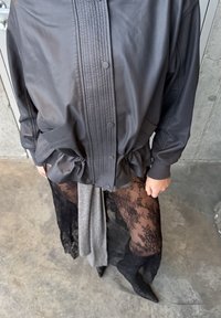 Veste en cuir noir avec patte boutonnée côtelée, taille cintrée et poches, associée à des leggings en dentelle noire transparente et des bottes noires à bouts pointus.