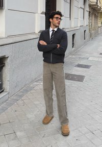 Veste zippée sombre par-dessus une chemise blanche et une cravate rayée ; pantalon en velours côtelé beige clair ; bottines marron ; debout sur un trottoir en ville.