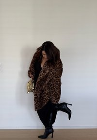 Ζεστό μαντίλι από ψεύτικη γουνοτυπία λεοπαρντάλη, μαύρο εφαρμοστό τοπ, μαύρες ψηλοτάκουνες μπότες και χρυσή τσάντα με παγιέτες. Λείο υλικό, υπερμεγέθης σχεδίαση.