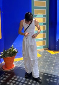 Pantalones cargo blancos con bolsillos, una blusa sin mangas blanca y botas negras hasta el tobillo. Una correa negra cuelga a través del torso, sosteniendo unas gafas.