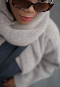 Μαύρα γυαλιά ηλίου υπερμεγέθους με κέλυφος χελώνας συνδυασμένα με ένα ελαφρύ γκρι πλεχτό κασκόλ, που τονίζει ένα υφασμάτινο ναυτικό ρούχο από κάτω.