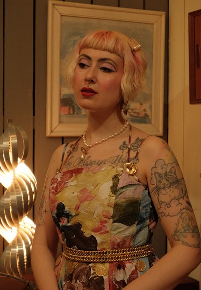 Vestido con estampado floral colorido y tejido texturizado. Cinturón de cadena dorada con acentos circulares, collar de perlas y pendientes de estilo vintage.