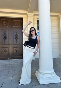 Black halter neck top, cream maxi skirt, sunglasses, and a black handbag. Standing next to a white column with wooden double doors in the background.