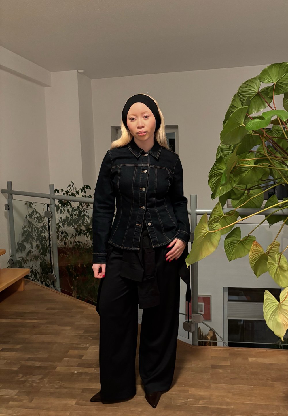 Schwarze Jeansjacke mit figurbetontem Schnitt, sichtbaren Nähten und Knöpfen; kombiniert mit lockeren schwarzen Hosen und einem schwarzen Haarband.