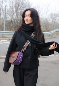 Svart kåpe med bred krage, kombinert med et mørkt skjerf med tekstur. Brun og lilla veske med reptilmønster og naglede detaljer.