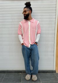 Camisa de manga curta xadrez vermelha e branca sobre uma camisola branca de manga comprida, combinada com jeans azuis largos e sapatos bege.