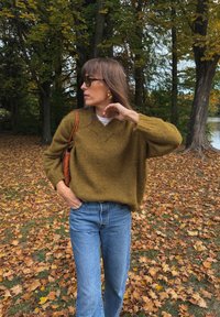 Olive rohelise värvi suur suurus, V-kaelusega kampsun, millele on sobitatud helesinised teksad. Aksessuaaride hulka kuuluvad prillid ja kootud pruun käekott.