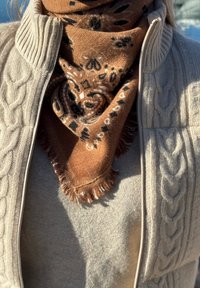 Gros plan sur une personne portant un pull à fermeture éclair beige en tricot torsadé et une écharpe brune à motifs enroulée autour du cou.