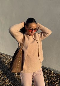 Pulôver e cardigan de malha em rosa claro com botões, combinados com calças coordenadas. Saco de camurça castanho com tachas douradas de lado.