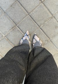 Chaussures pointues à imprimé serpent portées avec des chaussettes grises et un pantalon en jean foncé sur un trottoir en béton carrelé.