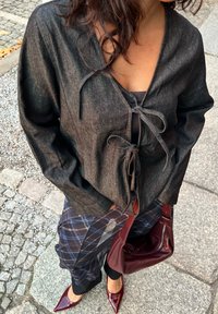 Mørkegrå omslagsbluse med knute foran, kombinert med rutemønstrede bukser. Vinrød håndveske og spisse hæler fullfører antrekket.