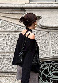 Μαύρη τοπ χωρίς ώμους, χαλαρή γραμμή, σε συνδυασμό με γκρι καρό σορτς. Αξεσουάρ περιλαμβάνουν μια μαύρη τσάντα και χρυσά κρίκα σκουλαρίκια. Φόντο από υφασμάτινο τοίχο.