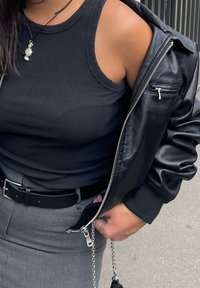 Μαύρη ριχτή αμάνικη μπλούζα κάτω από μια μαύρη δερμάτινη ζακέτα με ασημένια λεπτομέρεια στο φερμουάρ, συνδυασμένη με μια γκρίζα φούστα και μαύρη ζώνη.