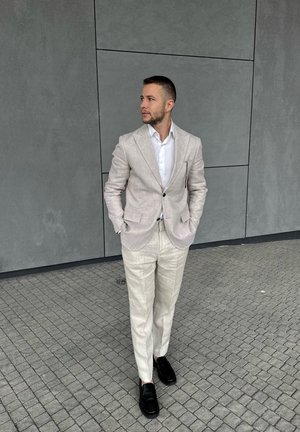 Blazer de lino color beige claro sobre una camisa blanca, acompañado de pantalones de lino beige claro y zapatos de cuero negros. Textura suave y corte ajustado.