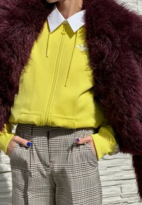 Sweatshirt amarelo com fecho e colarinho branco, combinado com calças xadrez de cintura alta. A camada exterior é um casaco de pelúcia falso de um vermelho bordô profundo.