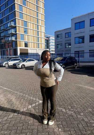 Top sin mangas beige sobre una camisa blanca de manga larga, combinado con pantalones de campana verde oliva y zapatillas de color claro, todo ello frente a un fondo urbano.