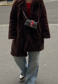 Καφέ ψεύτικη γούνα μπουφάν, κόκκινη μπλούζα, ανοιχτό μπλε παντελόνι με φαρδιά πόδια και μια μικρή μαύρη τσάντα με κόκκινες και ασημένιες λεπτομέ�ρειες, φορεμένη χιαστί.