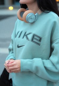 Lyseblå hettegenser med "NIKE"-logo, paret med beige og sølv over-ear hodetelefoner. Stoffets tekstur ser myk og koselig ut.