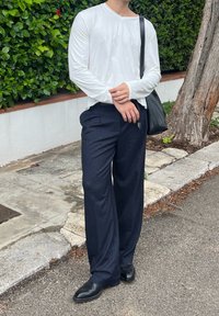 Hvid langærmet top med en let V-hals, parret med mørkeblå stribede bukser og sorte spidse sko, accessoriseret med en sort taske.