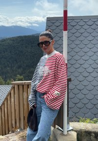 Rød og hvid stribet oversized sweatshirt med lange ærmer, parret med lyseblå høj talje jeans og en sort vævet håndtaske.