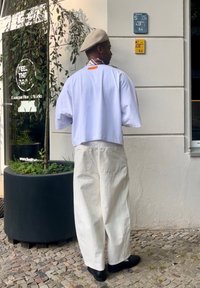 Lös passform vit kortärmad skjorta och krämfärgade vida byxor, matchade med svarta skor och en beige basker. Anmärkningsvärd kragdetalj.