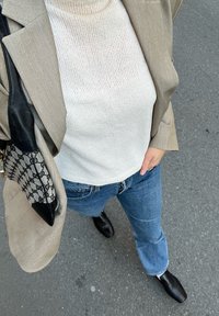 Μπεζ σακάκι, υφασμάτινη λευκή ζιβάγκο, μπλε τζιν με ελαφριά φαρδιά γραμμή και μαύρες μυτερές γόβες. Μαύρη τσάντα με σχέδιο.