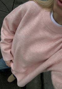 Maglione lavorato a maglia rosa chiaro con scollo rotondo a coste e vestibilità morbida. Texture soffice, spalle scese e cuciture visibili lungo i bordi.