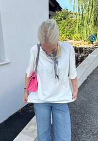 Camiseta de algodão branca com mangas curtas, bolso frontal, combinada com jeans de perna larga azul claro e uma pequena bolsa de ombro rosa.