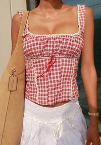 Rood-wit geruit crop top met ruffle schouderbanden, witte kantafwerking en een rode trekkoord. Gepaard met een witte textuur rok en een beige tas.