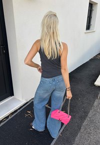 Bredde bukser i lys blå, grå ermeløs topp og en rosa quiltet veske med kjedehåndtak. Bakgrunnen har en hvit vegg.