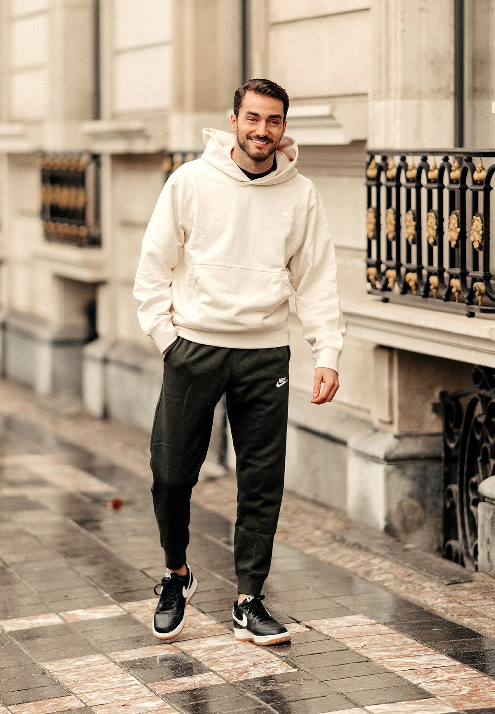 Sudadera crema con bolsillo canguro, joggers verde oscuro y zapatillas negras con detalles blancos. Diseño elegante y deportivo, adecuado para uso casual.