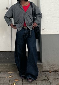 Szara koszula w szare paski na guziki, założona na czerwony top, do tego luźne ciemnoniebieskie dżinsy i ciemne buty. Dodatki to pasek i torebka.