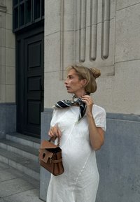 Brown handbag with a structured design and top handle, paired with a white textured dress and a black-and-white patterned scarf tied around the neck.