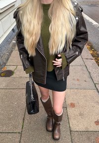 Bruine leren jas, groene gebreide trui, zwarte minirok, lange bruine laarzen met lichte accenten en zwarte gewatteerde handtas.