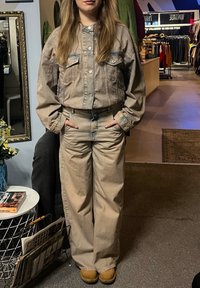 Beige denimjacka med knäppning och två bröstfickor, tillsammans med högmidjade, raka beige jeans. Skorna är bruna stövlar.