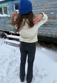 Pull en polaire à la texture crème, ample, jean noir évasé, et bonnet en laine bleu. Un porte-clés à fleur rose pend du jean.