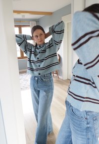 Maglione di lana a righe blu con design corto, caratterizzato da un collo alto e righe marrone scuro, abbinato a jeans a vita alta di colore azzurro chiaro.