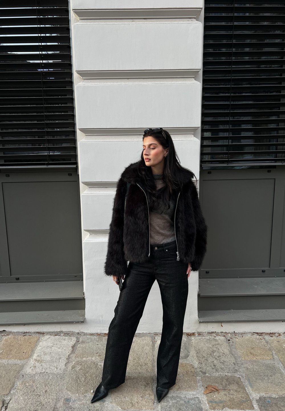 Svart faux fur-jacka med en cropped design, bärs över en texturerad brun topp, ihop med vida svarta jeans och spetsiga svarta klackar.