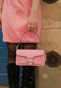 Ροζ δερμάτινη τσάντα χειρός με λεία φινίρισμα και ασημένιο κλείσιμο λογότυπου; διαθέτει κοντό λουρί και μια λεπτή υφα σμάτινη υφή.