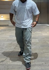 T-shirt oversized cinza claro com a estampa em relevo "67", combinada com jeans de denim azul claro. Ténis pretos com detalhes em vermelho e corrente.