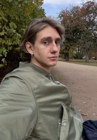 Roheline bomber-tüüpi jope tõmblukuga ees ja kahe küljetaskuga, kantud tumel sinisel särgil. Neutraalne taust, millel puud ja rada.