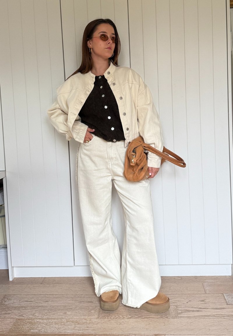White oversized denim jacket over a black button-up top, paired with cream wide-leg pants and brown platform boots. Brown shoulder bag and sunglasses.