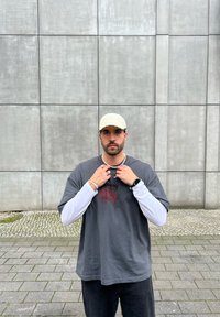 Γκρι υπερμεγέθη μπλούζα με γραφικό κόκκινου τριαντάφυλλου, σε επικάλυψη με λευκή μπλούζα με μακριά μανίκια. Αξεσουάρ περιλαμβάνουν ένα ανοιχτό καπέλο και κοσμήματα.