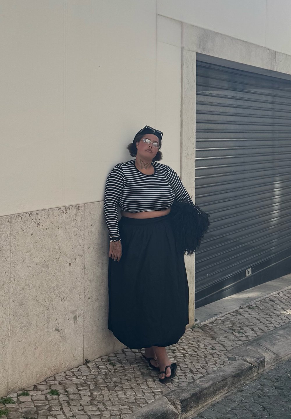 Jupe noire longue associée à un haut court à manches longues rayé noir et blanc. Des lunettes et un sac noir texturé complètent le look.