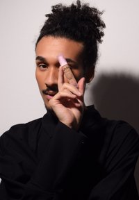 Sérum fond de teint NYX Bare With Me dans un tube transparent avec un capuchon rose. Le modèle le tient devant un fond uni, portant un haut noir.