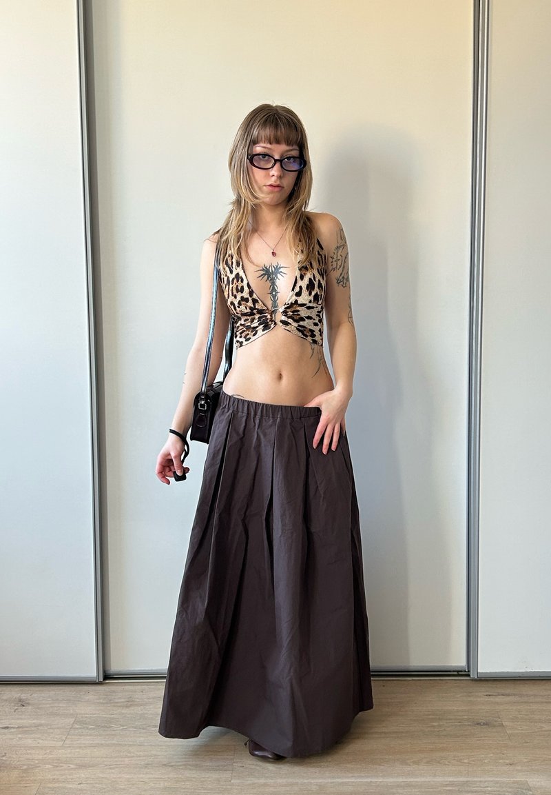 Jeune femme aux longs cheveux, portant un haut dos nu à imprimé léopard, une longue jupe sombre, des lunettes noires et portant un petit sac à épaule noir.