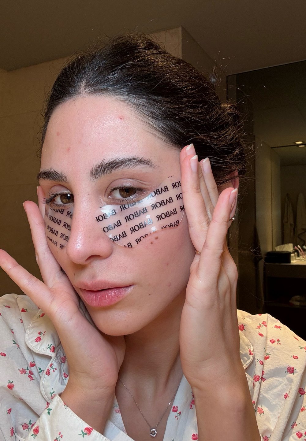 Klare Hydrogel-Augenmasken mit schwarzem Drucktext, unter den Augen aufgetragen. Die Haut wirkt glatt mit einem natürlichen, dewy Finish. Neutraler Hintergrund.