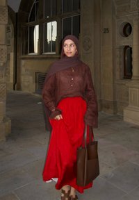 Ruda ilgomis rankovėmis palaidinė su mygtukais, raudona sluoksniuota sijonas, ruda rankinė ir rudi sandalai. Gėlių raštų hidžabas papildo aprangą.