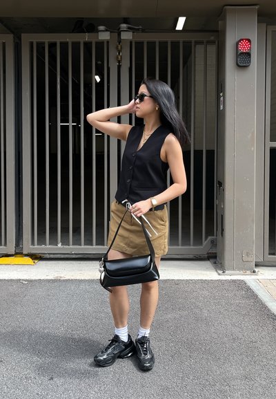 Chaleco negro ajustado con botones, minifalda marrón, bolso negro con herrajes plateados, zapatillas negras gruesas y calcetines blancos hasta el tobillo.